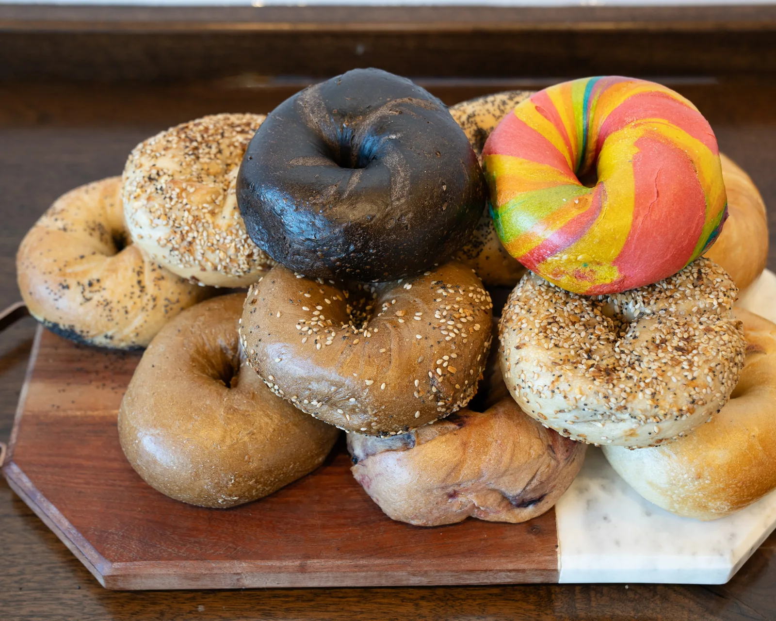 A stacked board of B's Bagels varieties including poppy, sesame, everything, pumpernickel, blueberry and the rainbow bagel